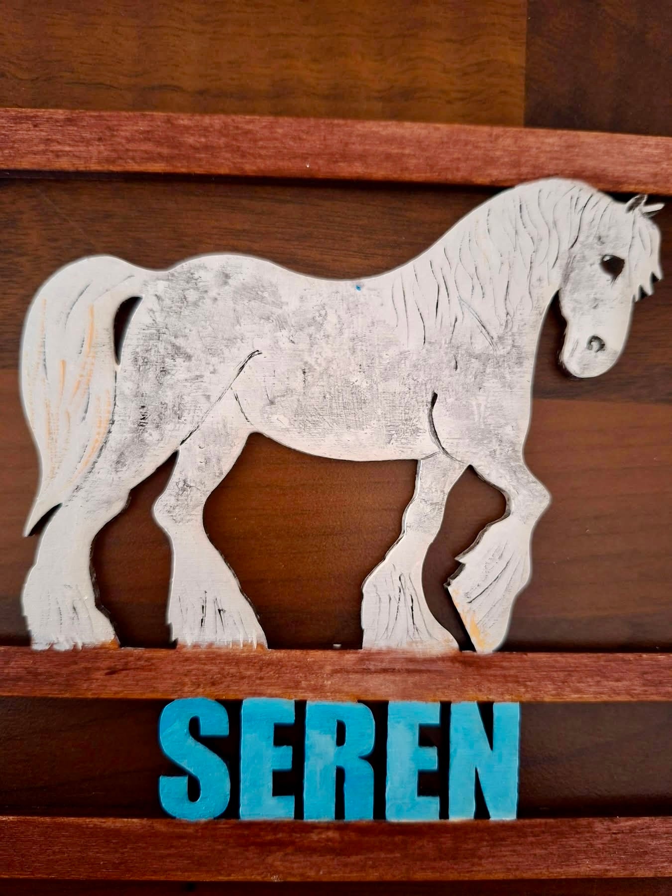 Wooden horse cutout on a wooden shelf with 'Seren' below