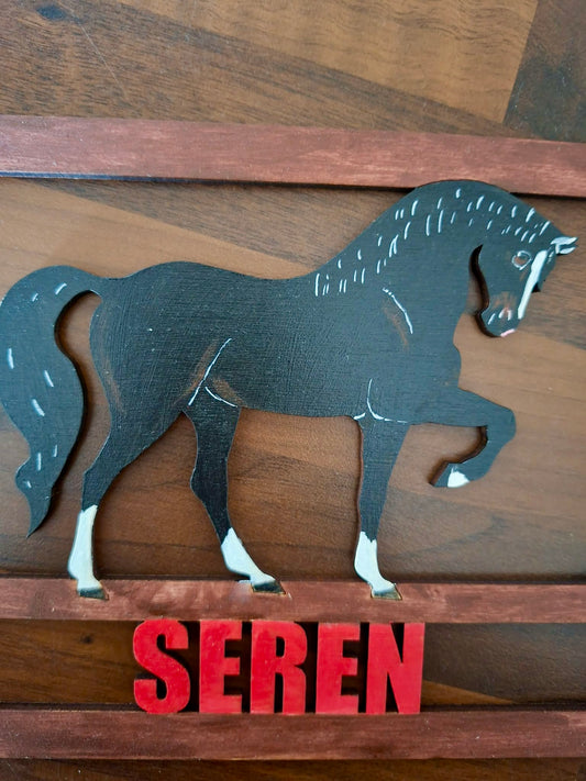 Metallic horse silhouette on a wooden background with 'Seren' text below